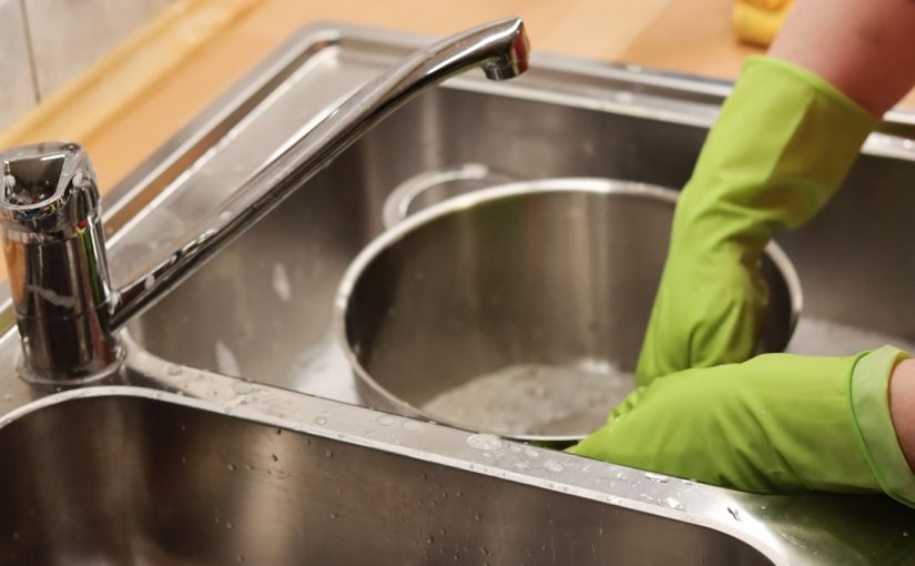 person in green shirt washing stainless steel sink